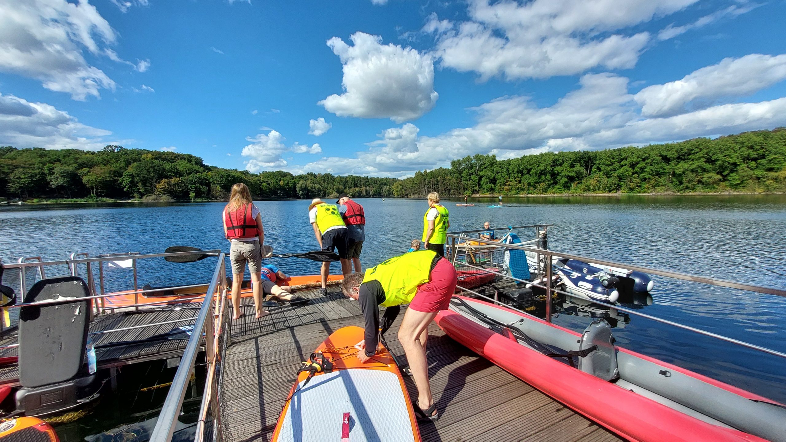 Gruppe in Schwimmwesten bereitet am Bootssteg Kajaks und SUP-Boards für die gemeinsame Ausfahrt vor.